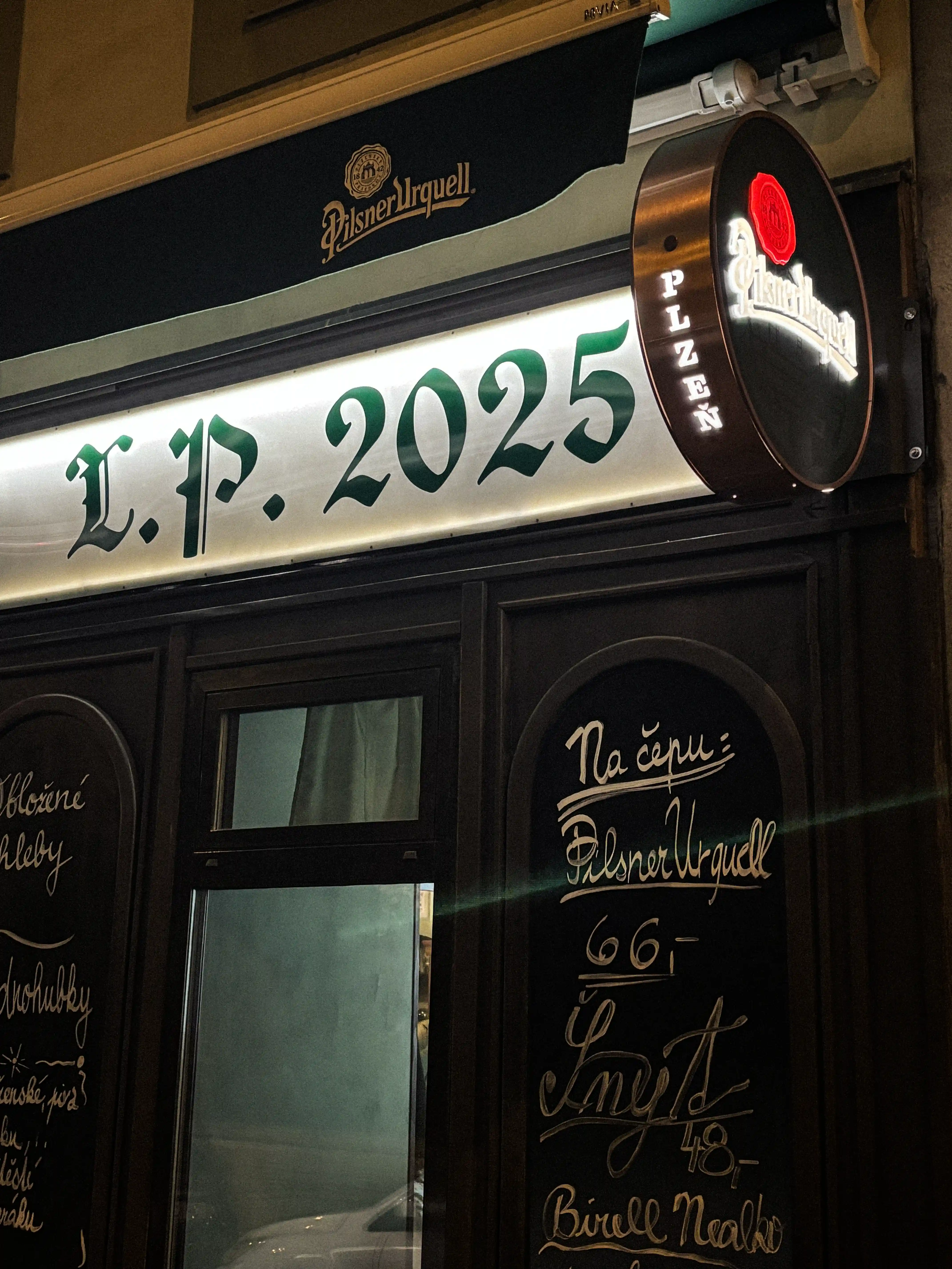 Exteriér hostince Školla, nápis L.P. 2025 a Pilsner Urquell