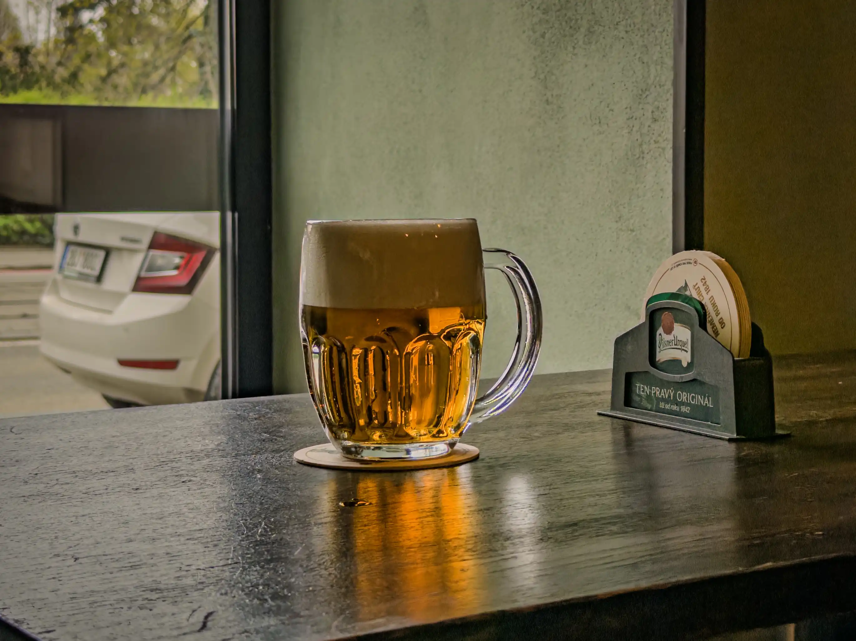 Sklenice Pilsner Urquell u okna s podtáckem Ten pravý originál v pivnici Školla